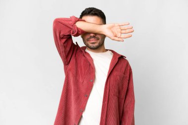 İzole edilmiş beyaz arka planda genç, yakışıklı beyaz bir adam. Gözlerini elleriyle kapatıyor.