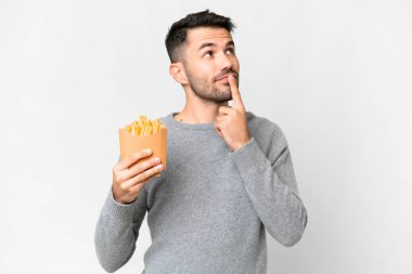 Young caucasian man holding fried chips over isolated white background having doubts while looking up