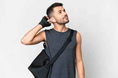 Young sport caucasian man with sport bag over over isolated white background having doubts and with confuse face expression