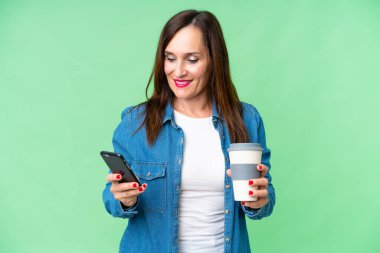 Orta yaşlı bir kadın izole edilmiş krom anahtar geçmişi var. Elinde kahve ve cep telefonu var.