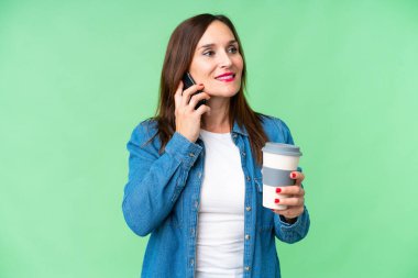 Orta yaşlı bir kadın izole edilmiş krom anahtar geçmişi var. Elinde kahve ve cep telefonu var.