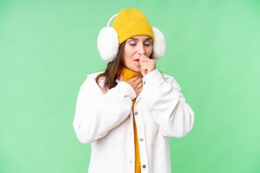 Middle age woman wearing winter muffs over isolated chroma key background is suffering with cough and feeling bad