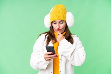 Middle age woman wearing winter muffs over isolated chroma key background thinking and sending a message