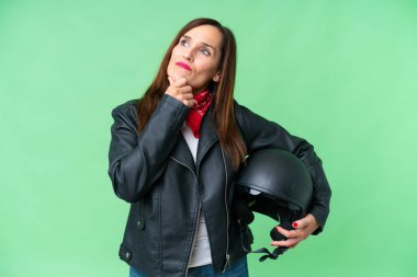 Middle age caucasian woman with a motorcycle helmet over isolated chroma key background having doubts