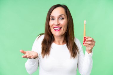 Middle age woman brushing teeth over isolated chroma key background with shocked facial expression