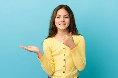 Mavi arka planda izole edilmiş küçük beyaz bir kız. Avucunun içinde hayali bir şey tutuyor. Bir ilan vermek için.