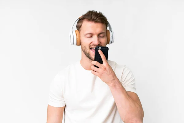 年轻英俊的高加索人男子胜过孤独的白人背景 一边用手机一边听音乐一边唱歌 — 图库照片
