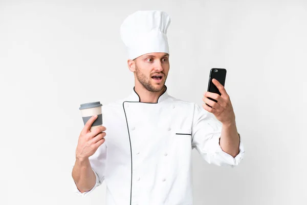 隔離された白い背景の上の若い白人シェフコーヒーを取り上げ モバイル — ストック写真
