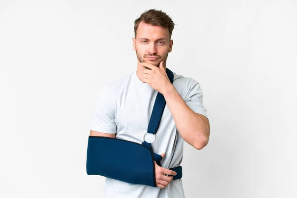 stock image Young caucasian man with broken arm and wearing a sling over isolated white background thinking