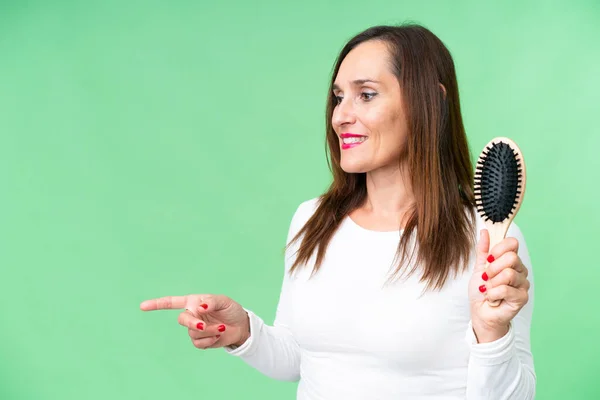 Middle age woman with hair comb over isolated chroma key background pointing to the side to present a product