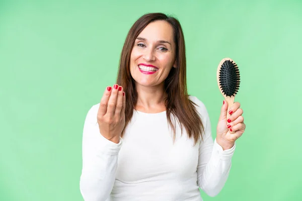 Middle age woman with hair comb over isolated chroma key background inviting to come with hand. Happy that you came