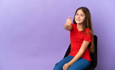 Little caucasian girl sitting on a chair isolated on purple background shaking hands for closing a good deal