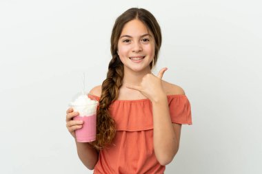 Little caucasian girl with strawberry milkshake isolated on white background making phone gesture. Call me back sign