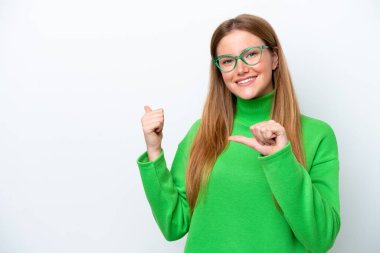 Beyaz arka planda izole edilmiş genç beyaz kadın bir ürünü sunmak için kenarı işaret ediyor.