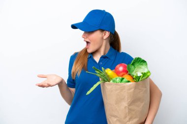 Young delivery woman taking a bag of takeaway food isolated on white background with surprise expression while looking side