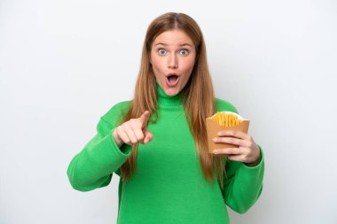Young caucasian woman holding fried chips isolated on white background surprised and pointing front