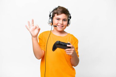 Beyaz arka planda video oyunu kontrolörüyle oynayan küçük beyaz çocuk parmaklarıyla işaret veriyor.