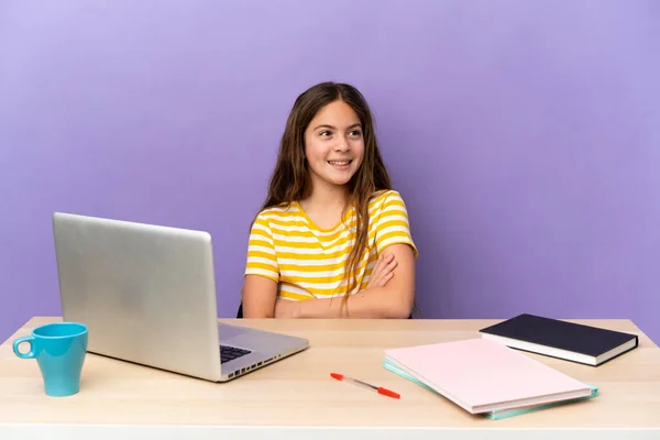 Little student girl in a workplace with a laptop isolated on purple background happy and smiling