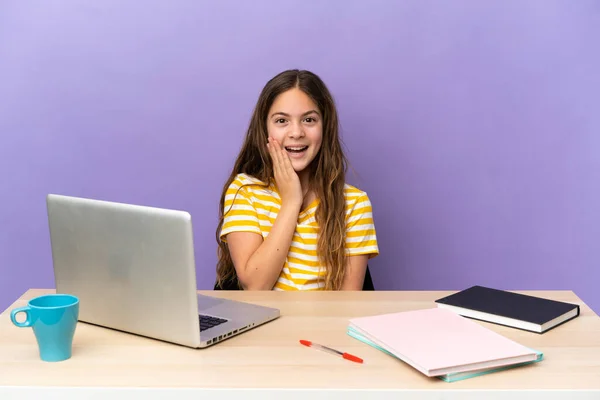 Little student girl in a workplace with a laptop isolated on purple background with surprise and shocked facial expression