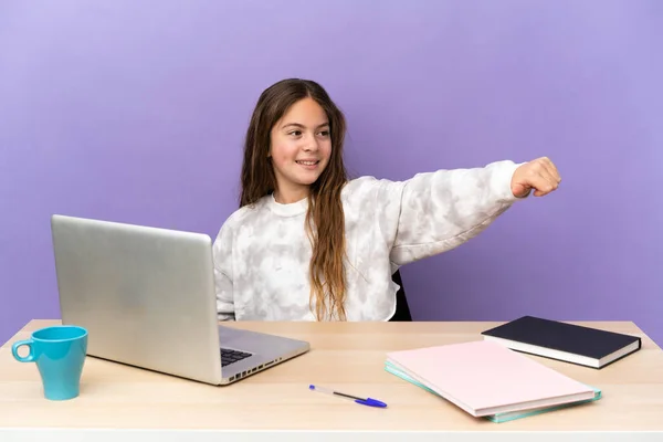Little student girl in a workplace with a laptop isolated on purple background giving a thumbs up gesture