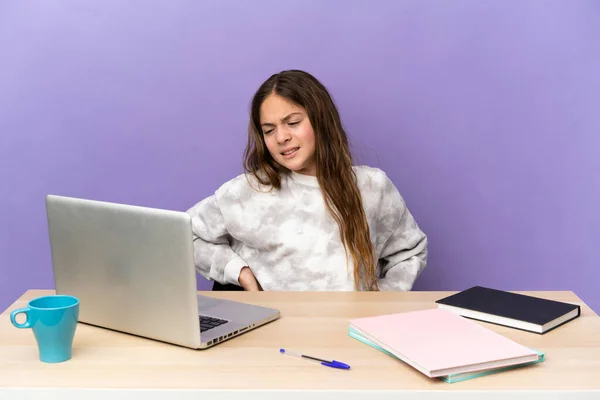 Little student girl in a workplace with a laptop isolated on purple background suffering from backache for having made an effort