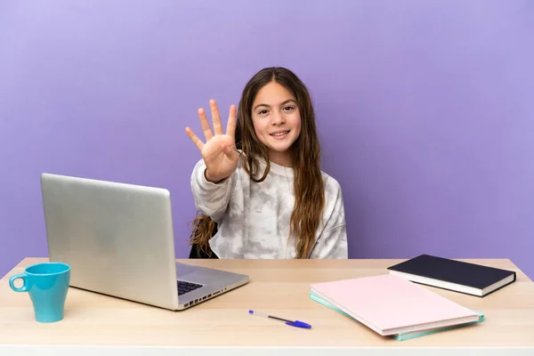Little student girl in a workplace with a laptop isolated on purple background happy and counting four with fingers