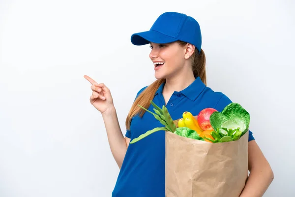 Young delivery woman taking a bag of takeaway food isolated on white background pointing finger to the side and presenting a product