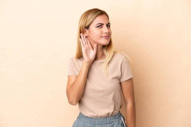 Sarışın Uruguaylı kız bej arka planda izole edilmiş. Kulağına elini sürerek bir şeyler dinliyor.