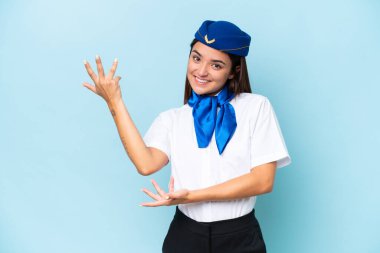 Airplane stewardess caucasian woman isolated on blue background extending hands to the side for inviting to come