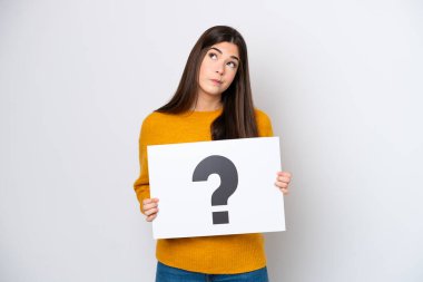 Beyaz arka planda izole edilmiş genç Brezilyalı bir kadın soru işareti olan bir pankart tutuyor ve düşünüyor.