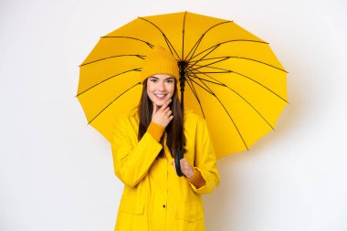 Young Brazilian woman with rainproof coat and umbrella isolated on white background happy and smiling