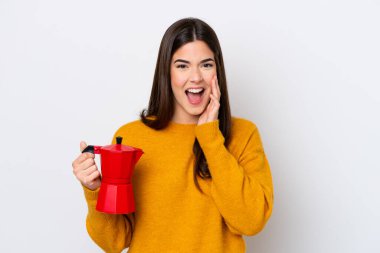 Young Brazilian woman holding coffee pot isolated on white background shouting with mouth wide open
