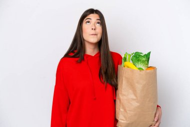 Bakkal çantası tutan Brezilyalı genç bir kadın beyaz arka planda izole edilmiş ve yukarı bakıyor.