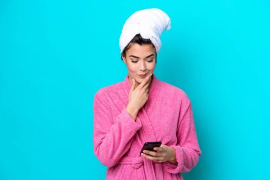 Young Brazilian woman with a bathrobe isolated on blue background thinking and sending a message
