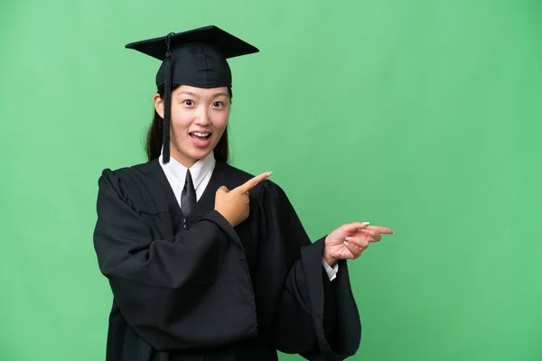 Young university graduate Asian woman over isolated background surprised and pointing side