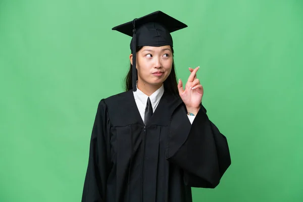 Young university graduate Asian woman over isolated background with fingers crossing and wishing the best