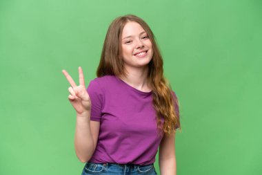 Genç ve güzel bir kadın, izole edilmiş arka planda gülümsüyor ve zafer işareti gösteriyor.