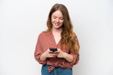 Beyaz arka planda izole edilmiş genç ve güzel bir kadın cep telefonuyla mesaj gönderiyor.