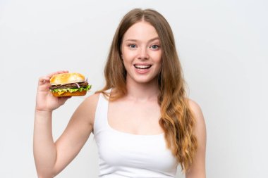 Young pretty woman holding a burger isolated on white background with surprise and shocked facial expression