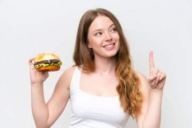 Young pretty woman holding a burger isolated on white background intending to realizes the solution while lifting a finger up