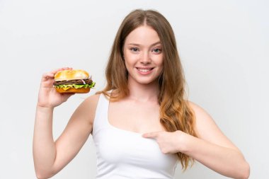 Beyaz bir arka planda yüzü sürpriz bir şekilde izole edilmiş hamburger tutan genç ve güzel bir kadın.