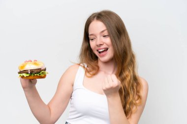 Genç, güzel bir kadın elinde hamburgerle beyaz arka planda zaferi kutluyor.