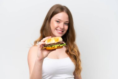 Genç, güzel bir kadın elinde hamburgerle beyaz arka planda mutlu bir ifadeyle.