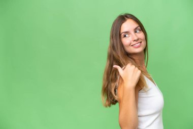 Tecrit edilmiş arka planda genç ve güzel bir kadın bir ürün sunmak için kenarı işaret ediyor.