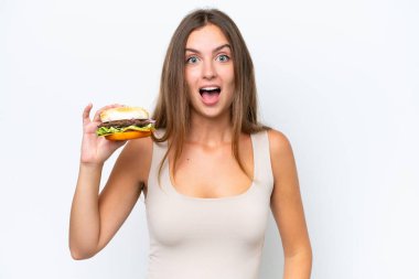 Young pretty woman holding a burger isolated on white background with surprise and shocked facial expression