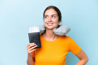 Young beautiful woman with Inflatable travel Pillow isolated on blue background posing with arms at hip and smiling