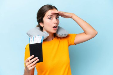 Young beautiful woman with Inflatable travel Pillow isolated on blue background doing surprise gesture while looking to the side