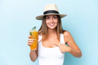 Young beautiful woman holding a cocktail isolated on blue background with surprise facial expression