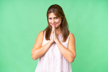 Middle age woman over isolated background keeps palm together. Person asks for something