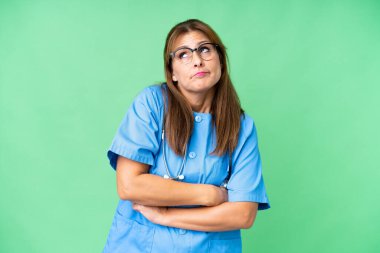 Middle age nurse woman over isolated background making doubts gesture while lifting the shoulders